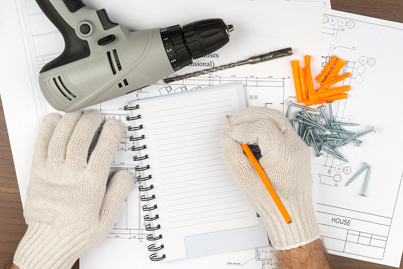 image of work-gloved hands writing in a notebook with tools on the table.